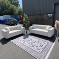 Two white sofas on a patterned rug in an outdoor setting with a building and car in the background.